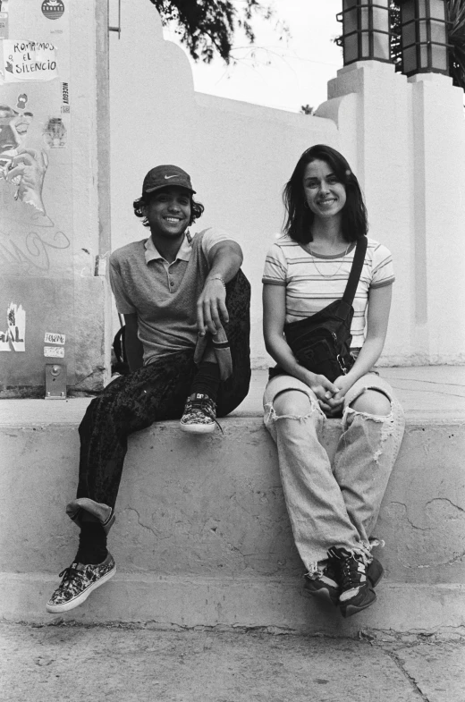 two young people sitting on the side of a building