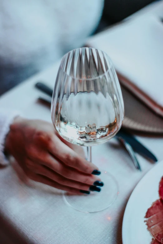 a hand holding a wine glass on top of a white table