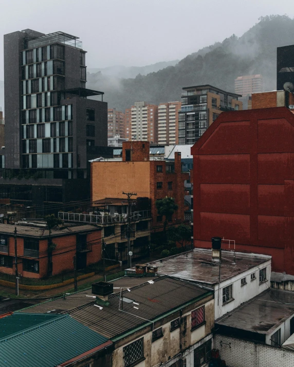 tall buildings, and one building with the top part in red, are shown in front of a cloudy mountain