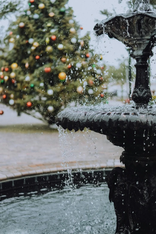 an illuminated fountain with lots of water in front of a christmas tree