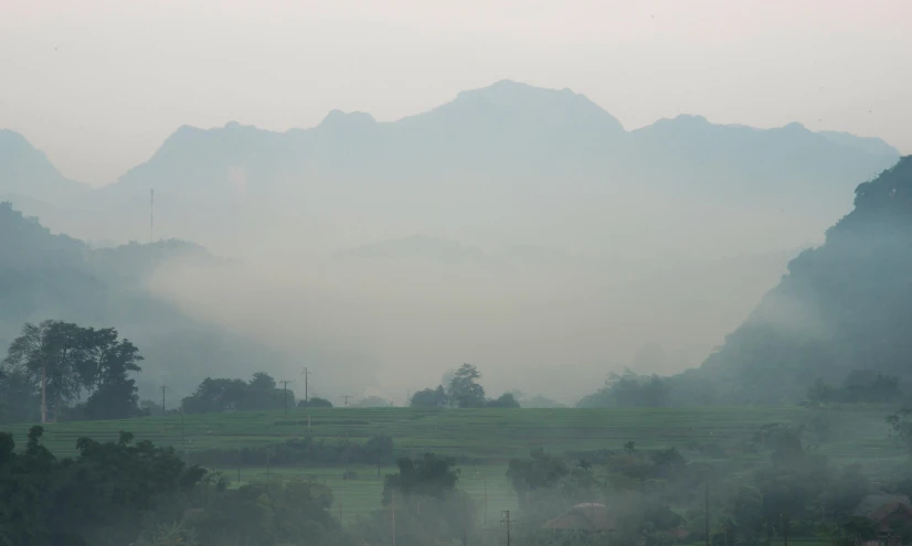 a foggy view of a grassy field, hills and mountain