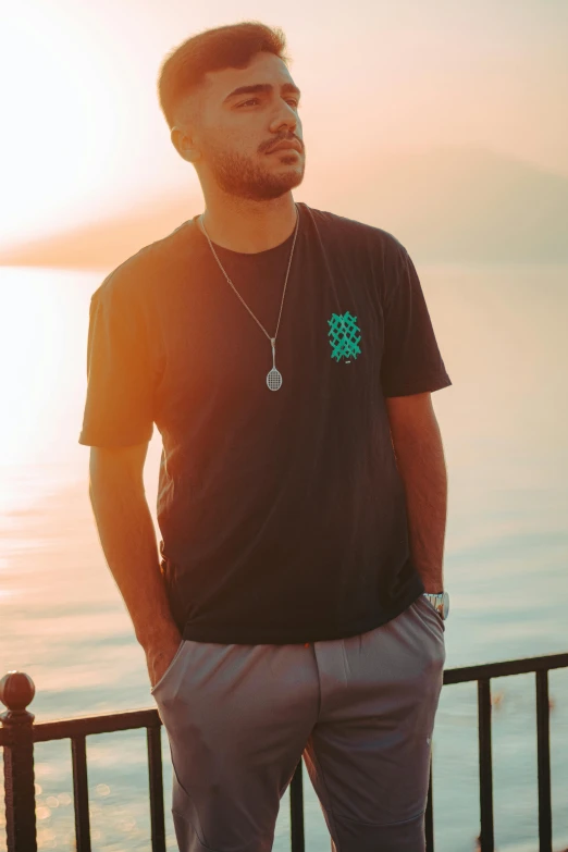 a man standing near a body of water wearing a shirt with a turtle symbol on it