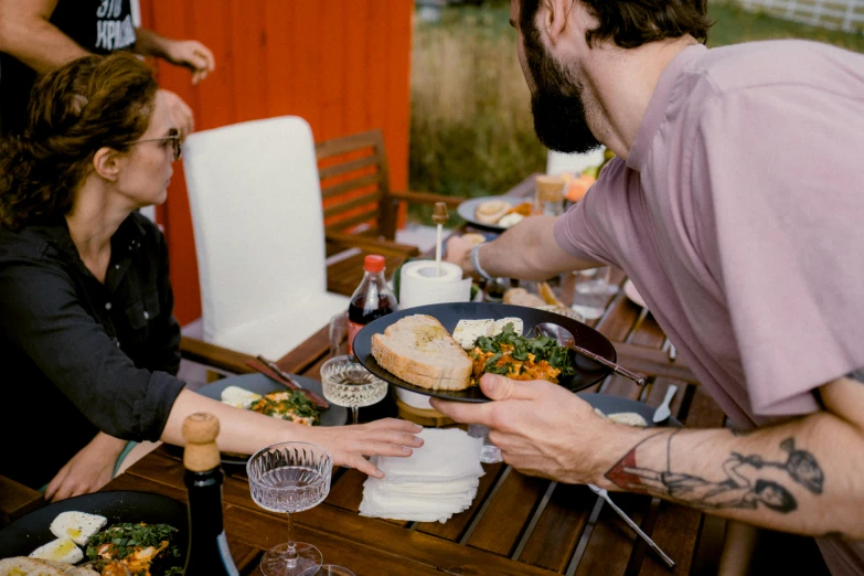 a group of people sitting around a wooden table covered with plates and bowls of food