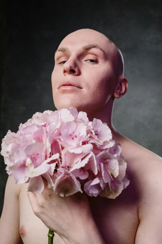 a shirtless man holds a flower in front of his face