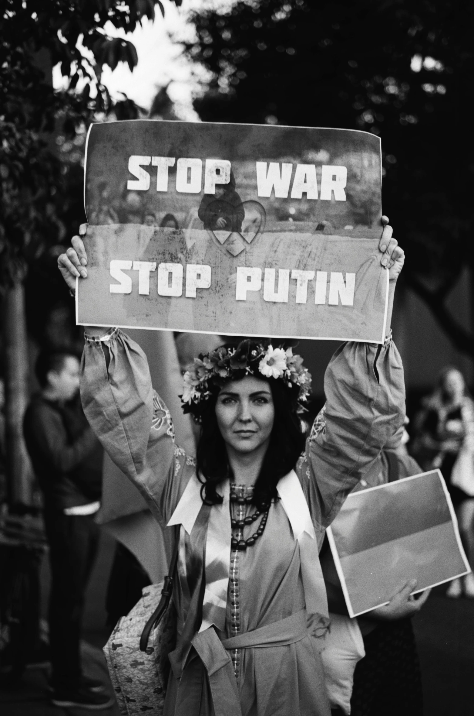 woman wearing flower wreaths and holding up sign that says stop war