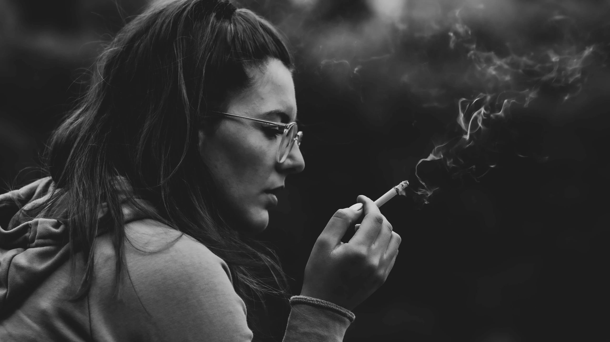 a woman in glasses holding a cigarette in her hand