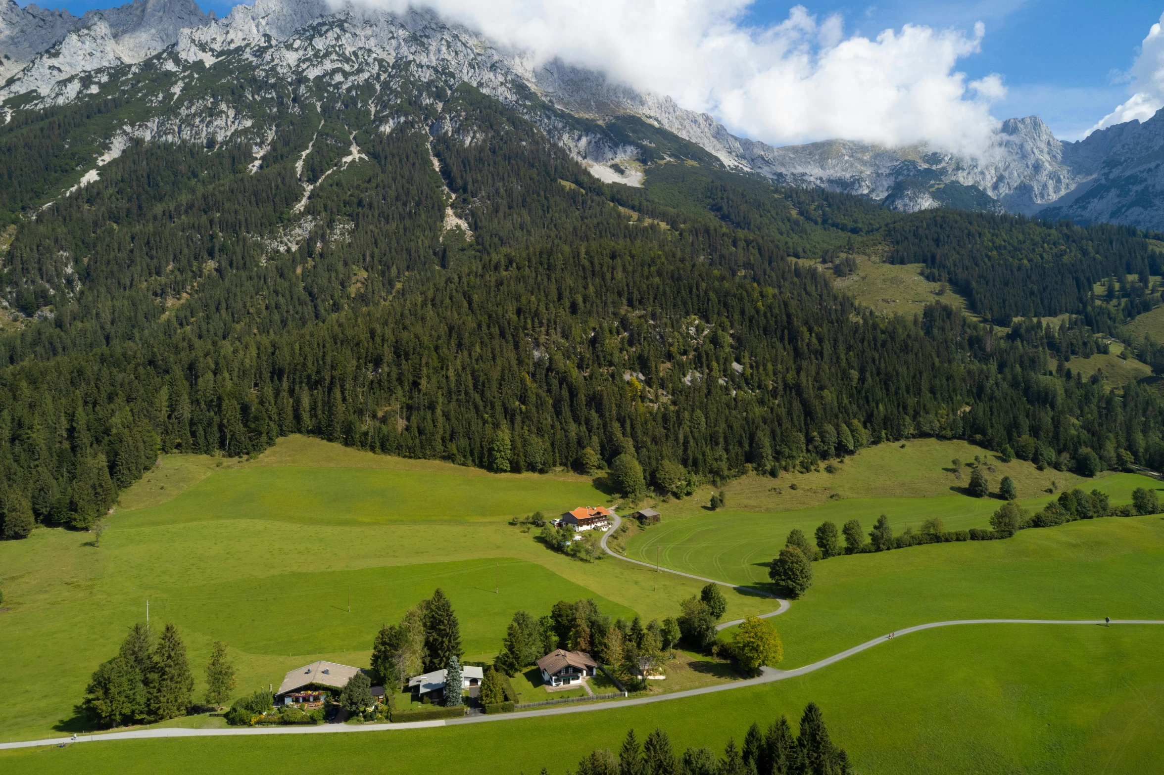 a mountain with a house, cars, trees and clouds