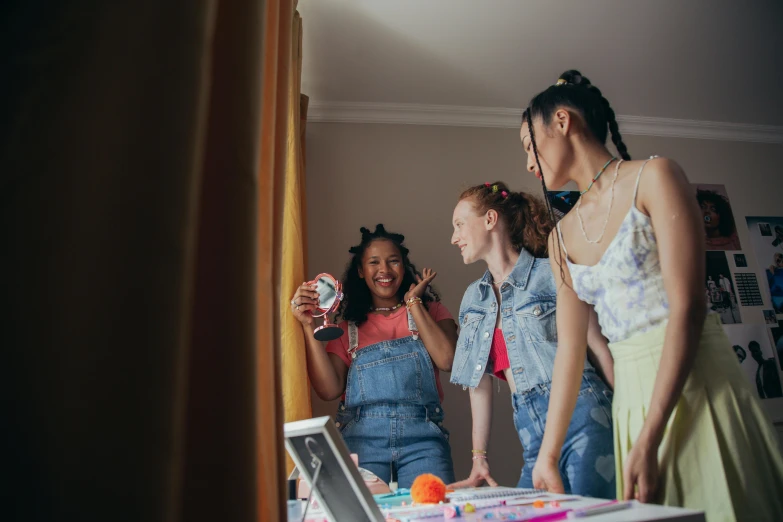 four girls looking in a mirror, with the girl standing and laughing