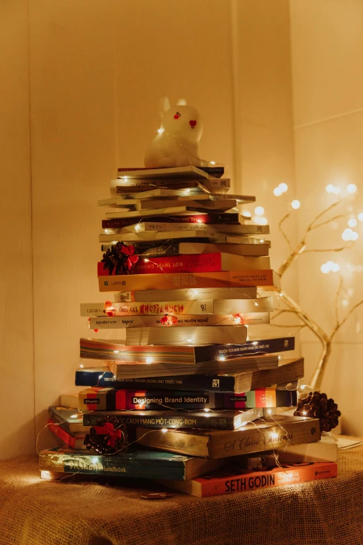 a stack of books sits on a counter in front of a lighted tree