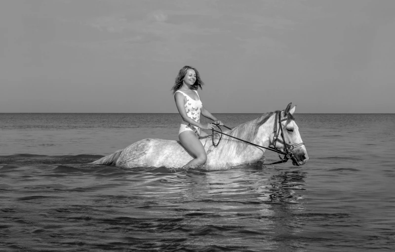 a beautiful woman in white bathing suit riding on the back of a horse