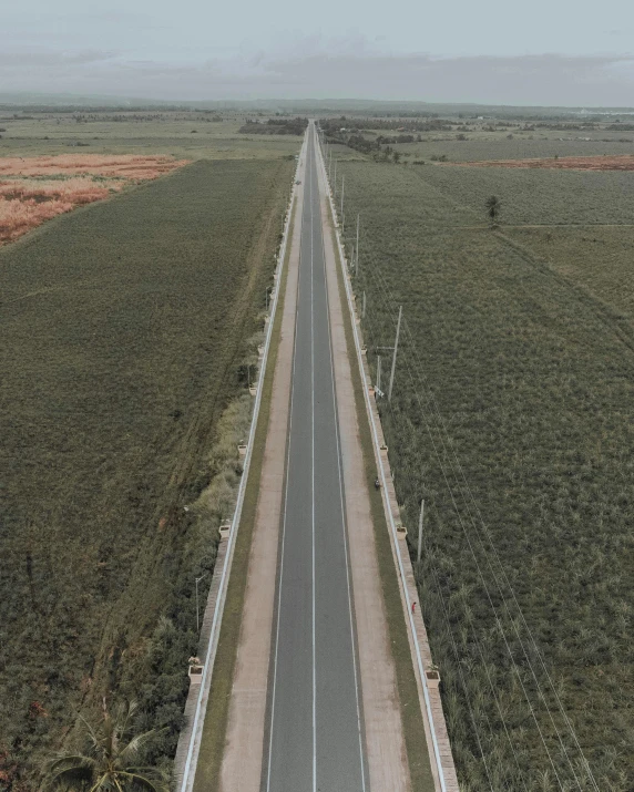 a view of a long road in the middle of a green plain