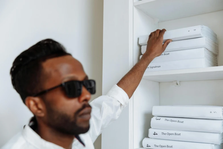 man wearing sunglasses reaching up and placing folded paper on white shelf