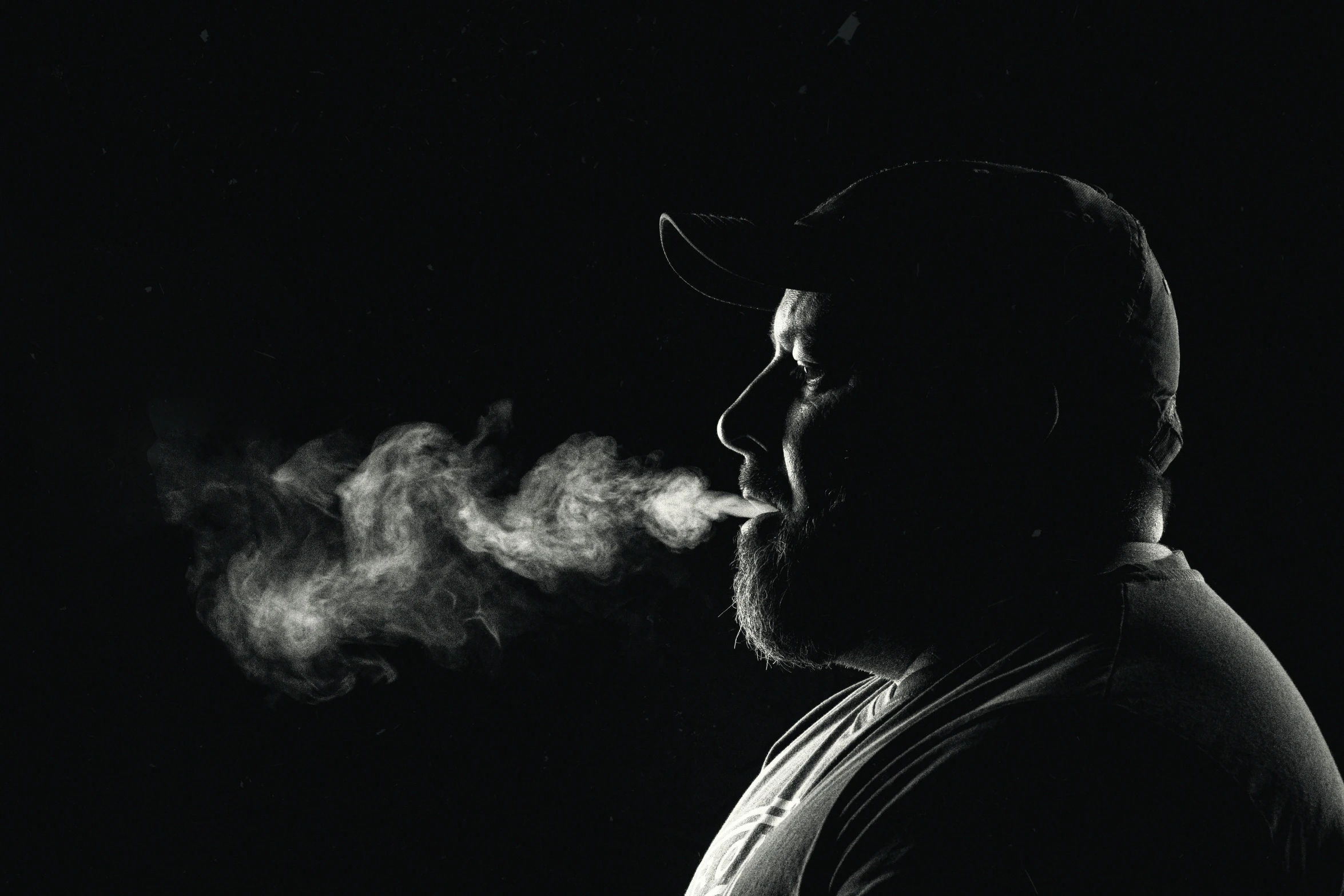 a man wearing a hat blowing smoke into his face