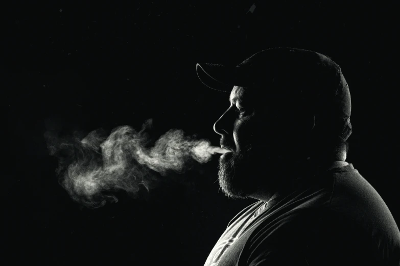 a man wearing a hat blowing smoke into his face