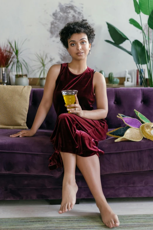 a beautiful young woman holding a cup of beverage sitting on a couch