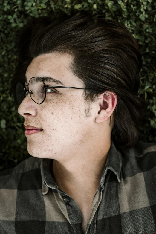 a boy with glasses stares down in front of a hedge