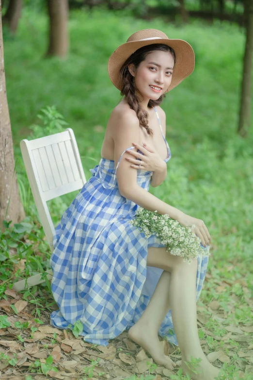 woman in blue dress and straw hat sitting on a bench