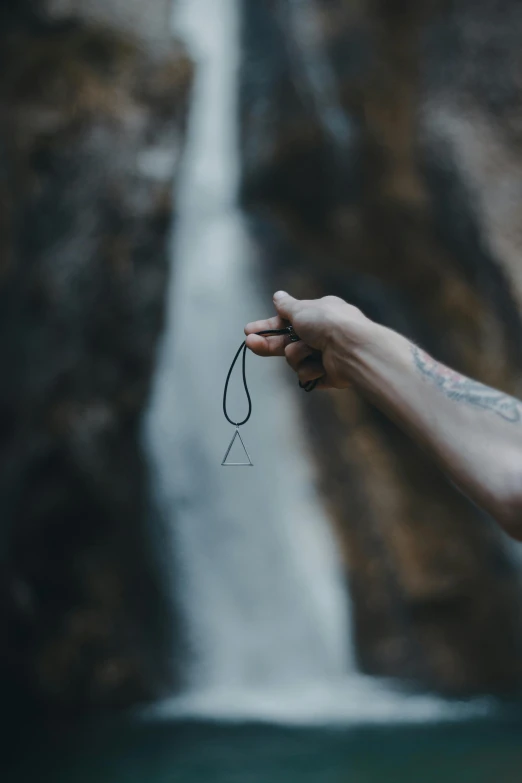 a person holds their fingers up near a waterfall