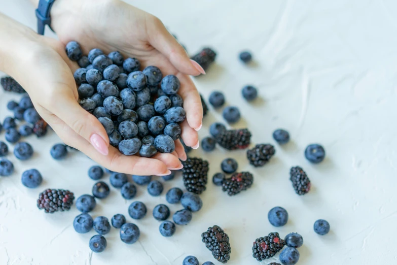 a person is holding some blueberries and raspberries on the table