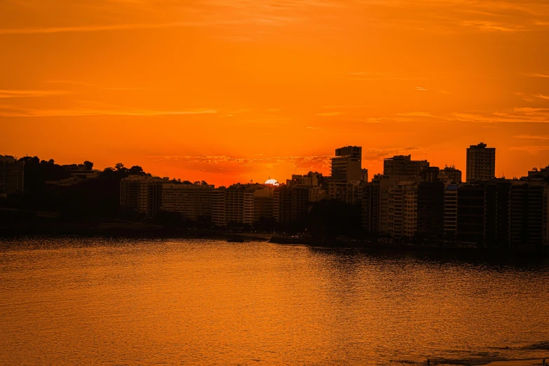 an orange sunset and the silhouette of some buildings against the horizon