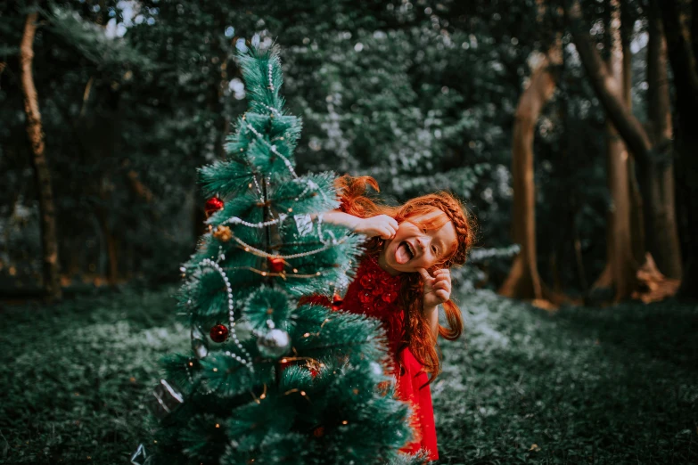 red haired girl reaching out to the bottom of a christmas tree