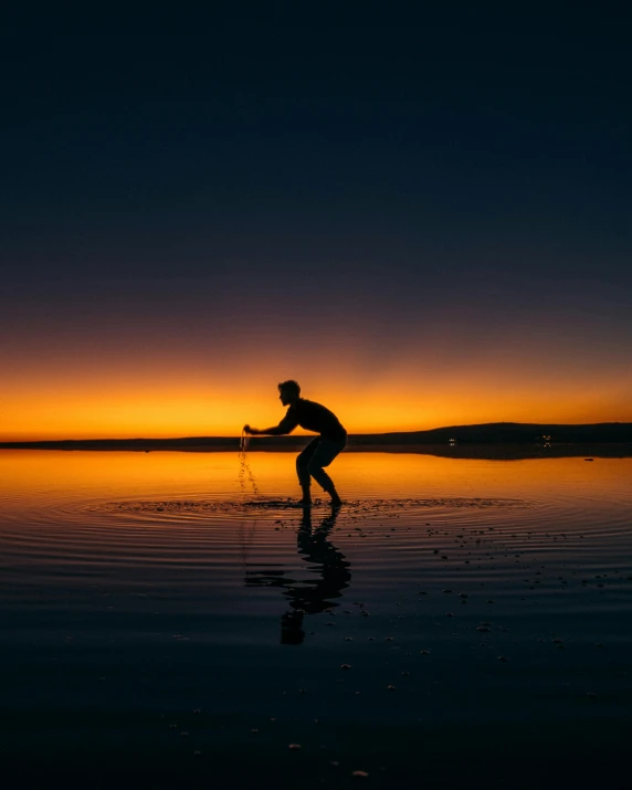 man stands on his surf board as the sun sets