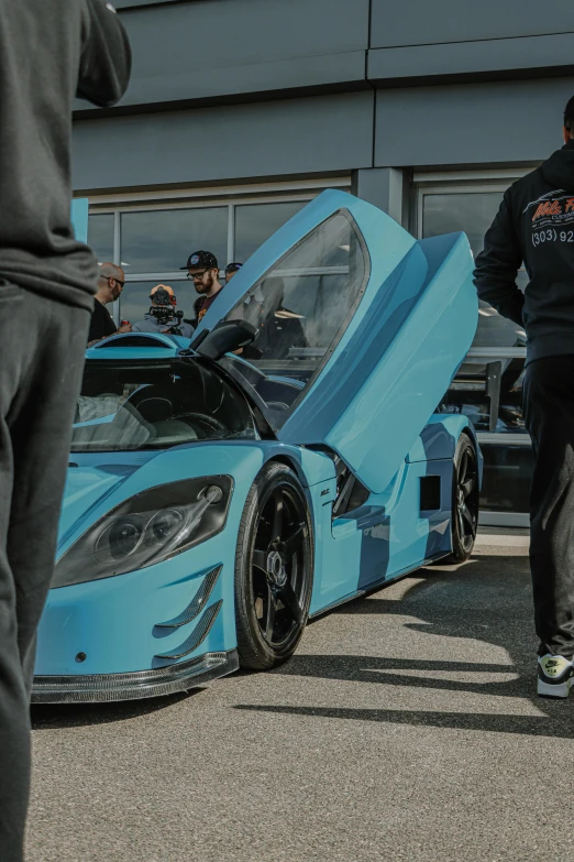 a blue sports car parked in front of a group of people