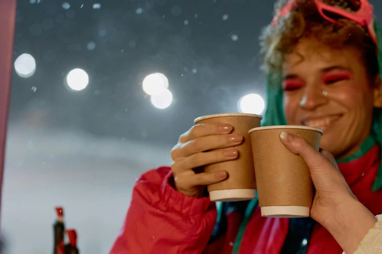 woman in red jacket holding up a paper cup with coffee inside