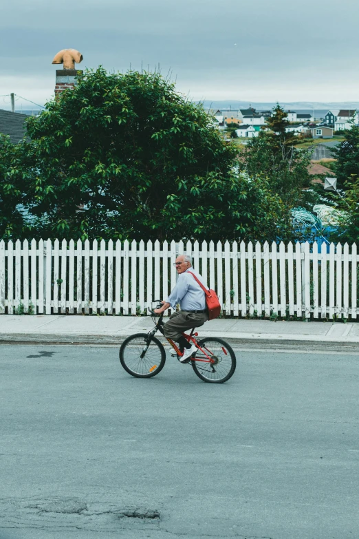 man on bicycle riding through the intersection near white picket fence