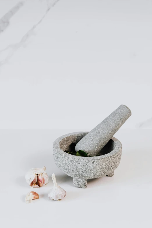 a mortar bowl filled with garlic next to a piece of garlic on the ground