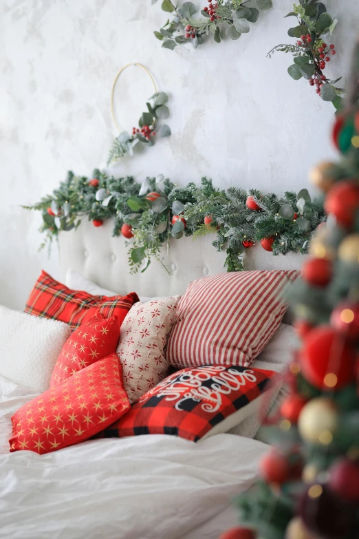 a bed with red and white pillows near a christmas wreath