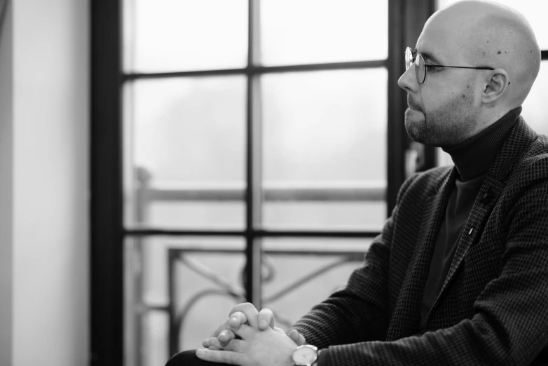 black and white pograph of a bald man looking out a window