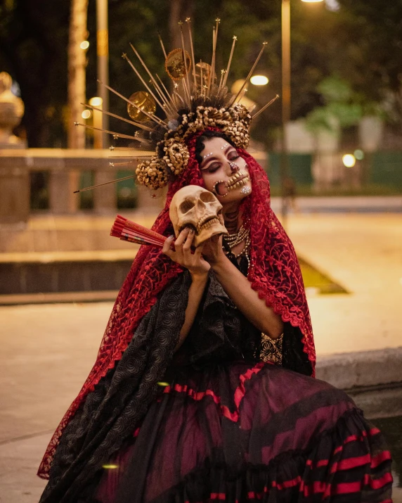 a woman with makeup, skeleton head, and red gown holding a skull