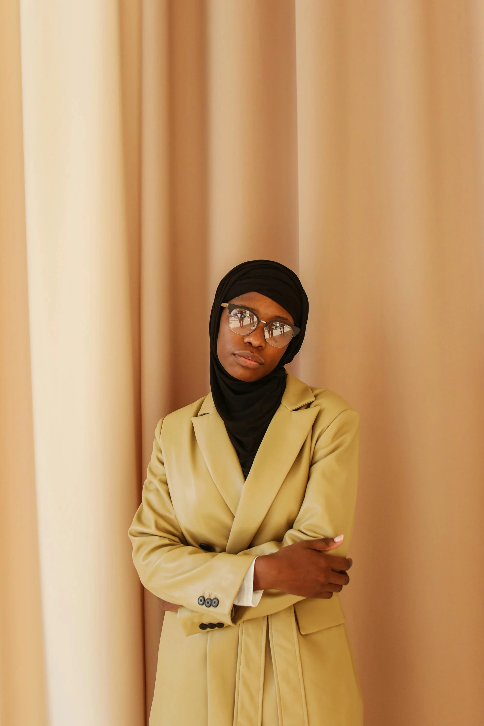 a woman standing behind a curtain in a black tie and tan suit