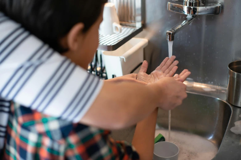 woman washing hands at kitchen sink next to drinking water