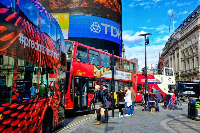 people are boarding and standing around two double decker buses