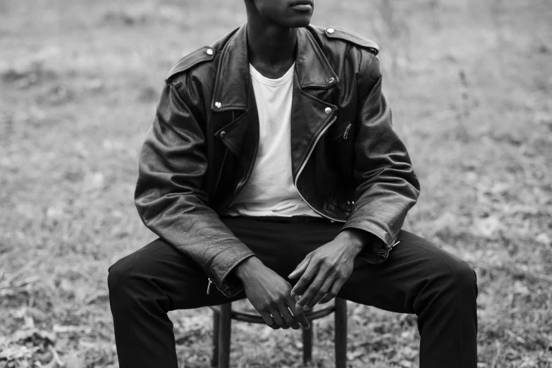 a young man sitting in a chair while wearing a jacket