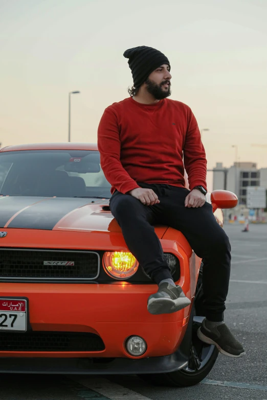 a man in a black beanie sits on top of an orange sports car