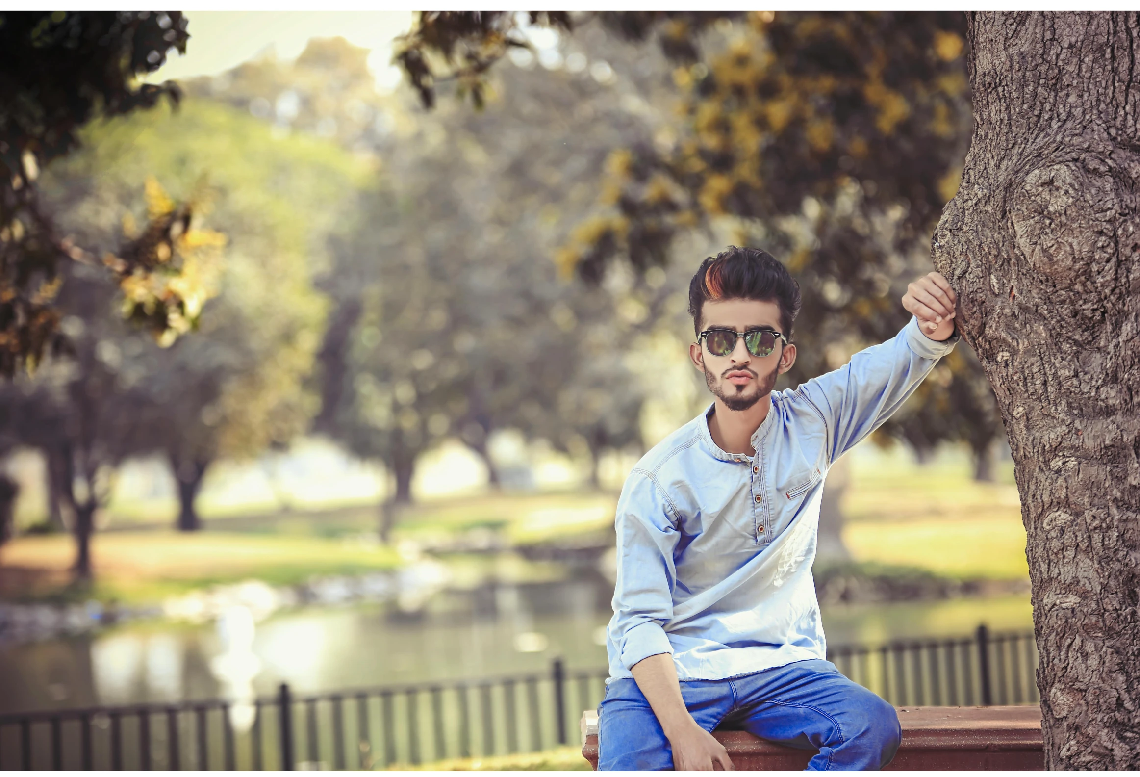 the young man in glasses is posing by the tree