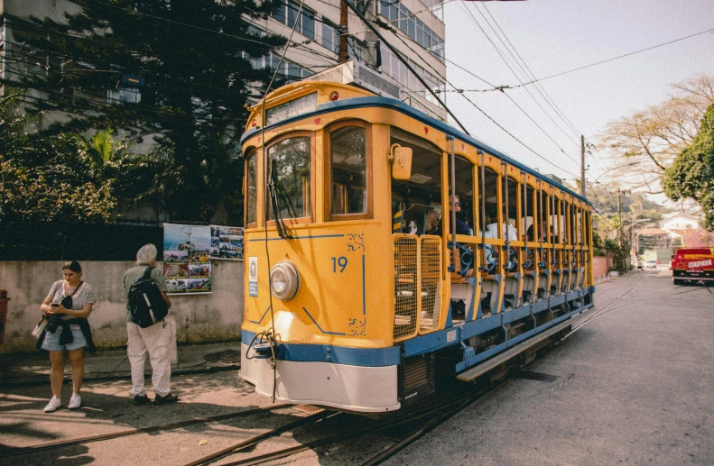 a yellow trolly car stopped at a street corner with tourists
