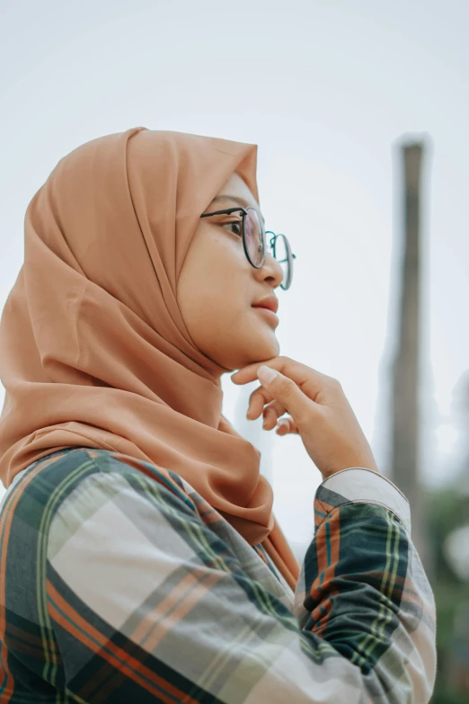 a woman in a headscarf and glasses looks off into the distance