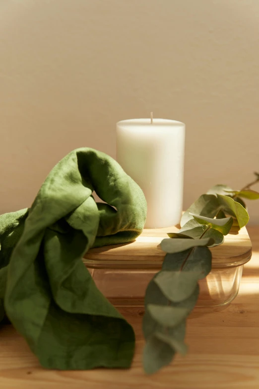 a candle, silk scarf and green leaves on a table