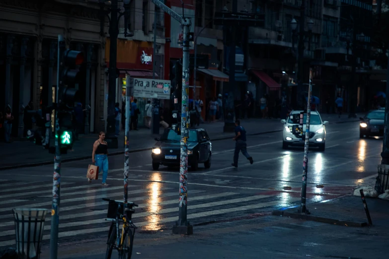 a car with its headlights on and a van and people crossing the street in the rain at night