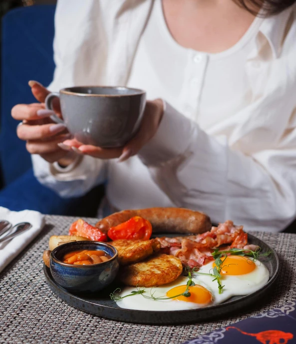 a person with a coffee cup, fried eggs and other foods