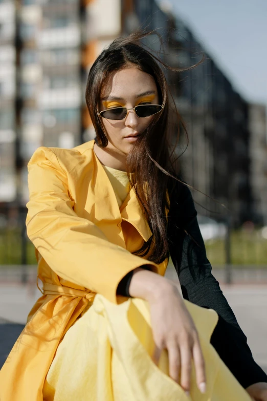 a woman with long hair sitting on a bench wearing yellow dress