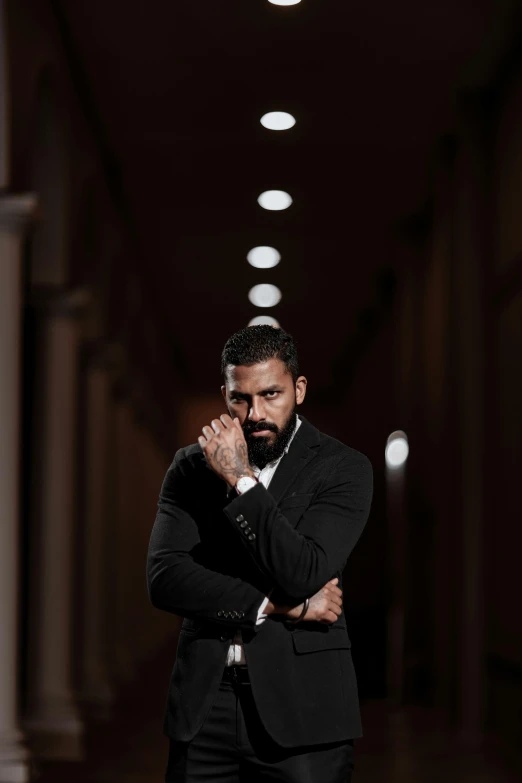 a bearded man in black suit standing with his arms folded