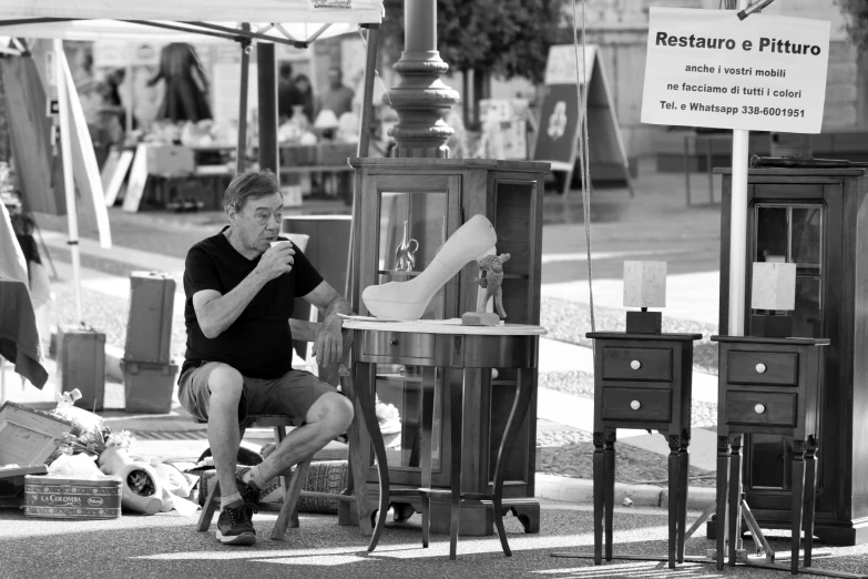 a man sitting on a chair eating soing in front of an old market