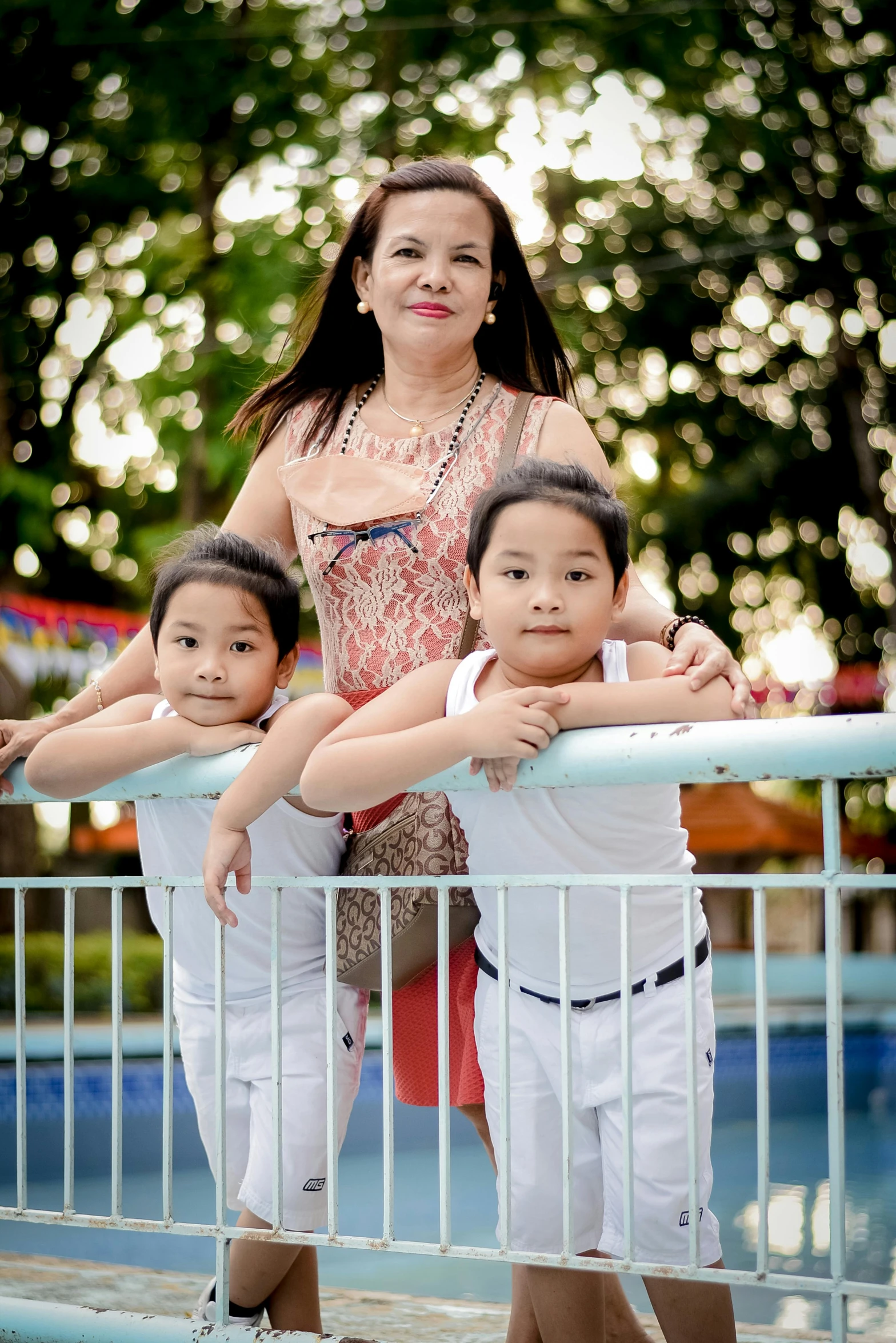 an adult and two children stand on a railing in front of a pool