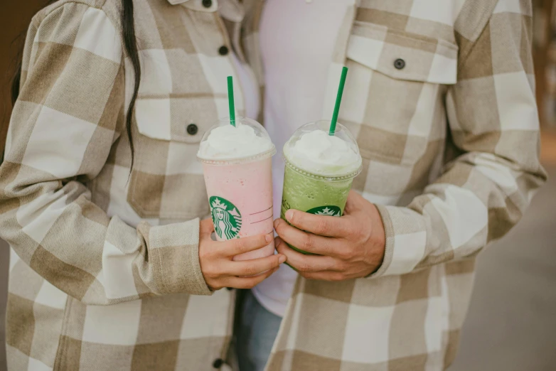 someone holds two pink drinks with starbucks's logo on them