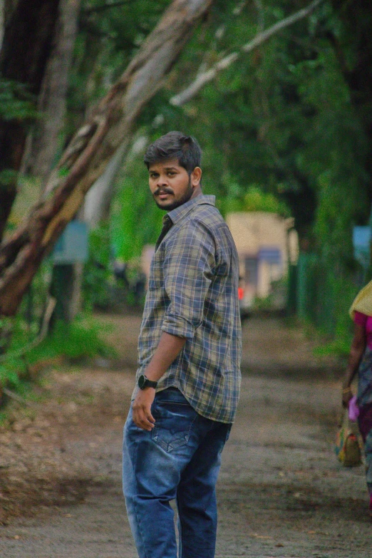 a man walking along a dirt path wearing a plaid shirt